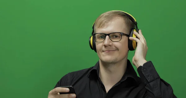 Guy luistert naar muziek in een draadloze gele hoofdtelefoon. Groen scherm — Stockfoto