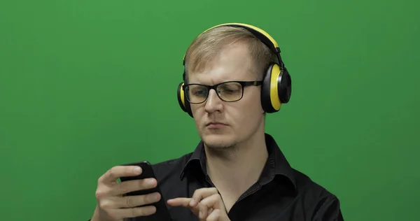 Um tipo a usar um telefone inteligente em auscultadores amarelos sem fios. Tela verde — Fotografia de Stock