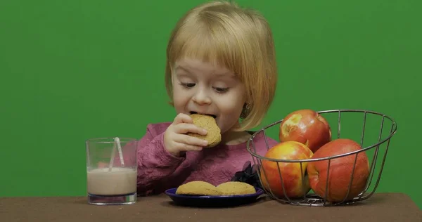Girl sitting at the table with apples, cacao and eating cookies. Chroma Key