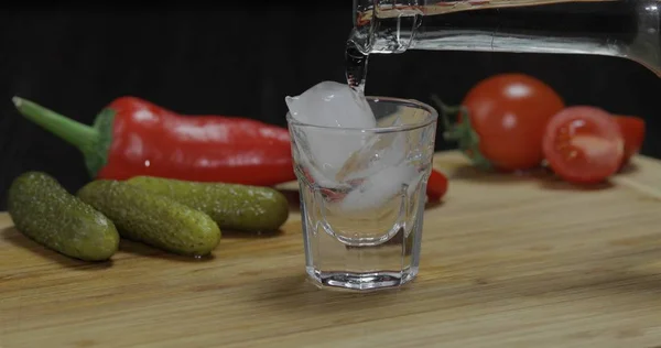Vierta el vodka de una botella en un vaso de chupito con hielo sobre la mesa —  Fotos de Stock