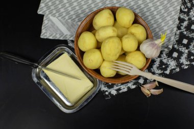 Yıkanmış taze patates pişirmeye hazır masada. Tereyağı, sarımsak, ahşap çatal