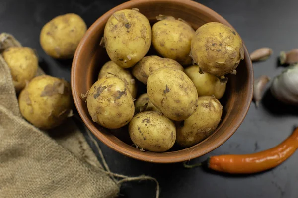 Dirty raw potatoes on a plate on table with garlic and pepper