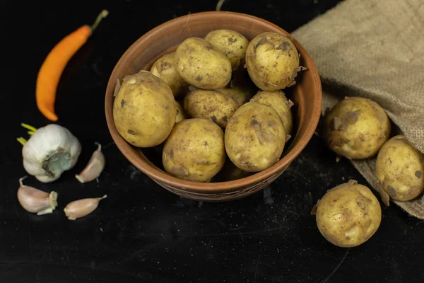 Dirty raw potatoes on a plate on table with garlic and pepper