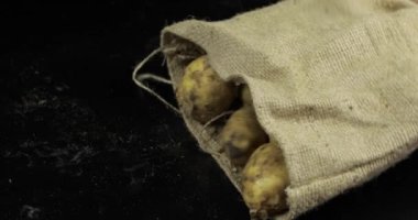 Patates tuval çantadan siyah surfase düşüyor. Bir kazık taze çiğ patates