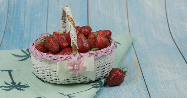 Strawberries in a small basket on the blue wooden background. Place for text