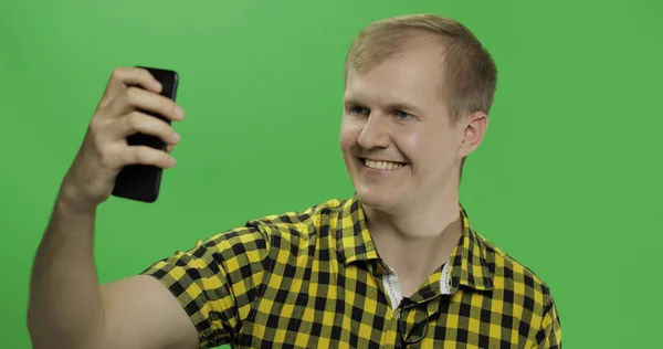 Hombre joven caucásico en camisa amarilla tomando bonitas selfies en el teléfono inteligente — Foto de Stock