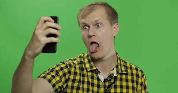 Hombre joven caucásico en camisa amarilla tomando divertidas selfies en el teléfono inteligente — Foto de Stock