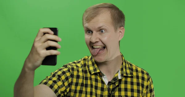 Hombre joven caucásico en camisa amarilla tomando divertidas selfies en el teléfono inteligente — Foto de Stock