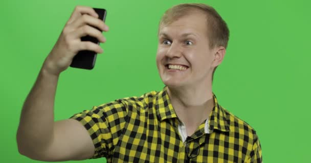 Белый молодой человек в жёлтой рубашке делает красивые селфи на смартфоне — стоковое видео