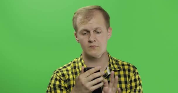 Homme caucasien en chemise jaune défilant, textos sur le smartphone dans ses mains — Video