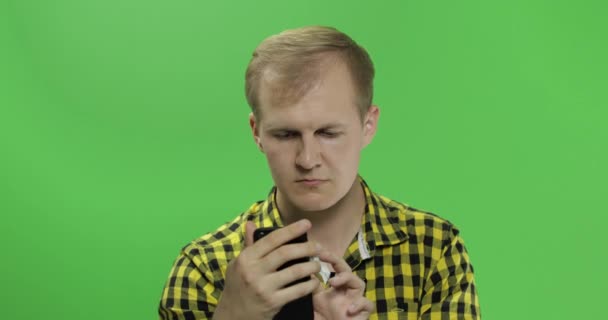 Caucasian man in yellow shirt scrolling, texting on the smartphone in his hands — Stock Video