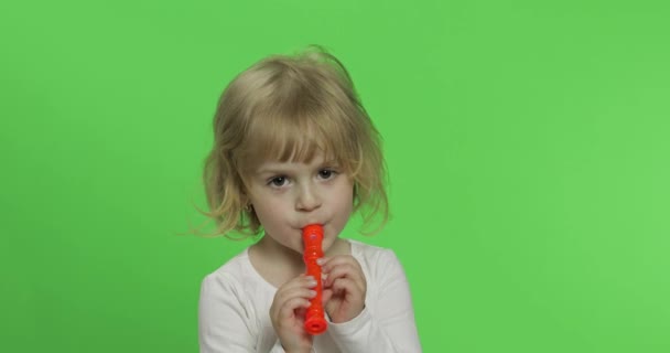 Portrait of three years old blonde girl plays on toy pipe on green background — Stock Video