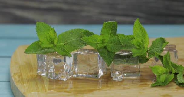 Кубики льоду і листя м'яти ізольовані на дерев'яній обробній дошці — стокове відео