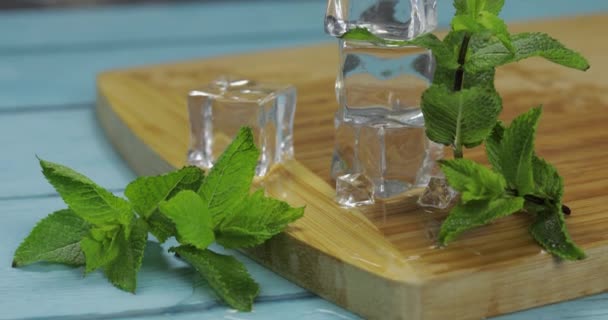 Cubos de hielo y hojas de menta aisladas en tabla de cortar de madera — Vídeo de stock