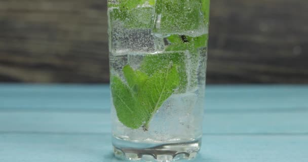 Чистая вода в стакане с зелеными листьями мяты и кубиками льда — стоковое видео