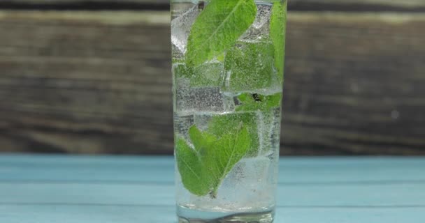 Agua clara en vidrio con hojas de menta verde y cubitos de hielo — Vídeo de stock