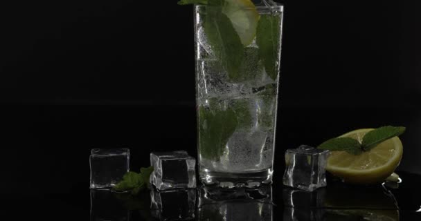 Прозора вода в склі з зеленим листом м'яти та кубиками льоду на чорному тлі — стокове відео