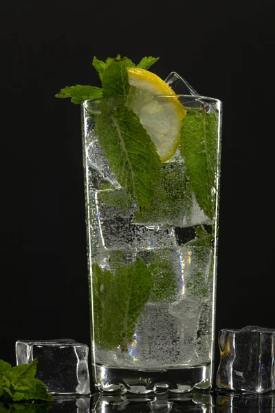 Agua clara en vidrio con hojas de menta verde y cubitos de hielo sobre fondo negro —  Fotos de Stock