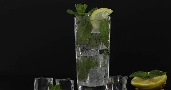 Helder water in glas met groene muntblaadjes en ijsblokjes op zwarte achtergrond — Stockfoto