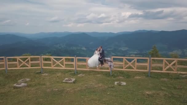 Lugar com noiva sentar-se na cerca perto de colinas de montanha. Drone aéreo disparado — Vídeo de Stock