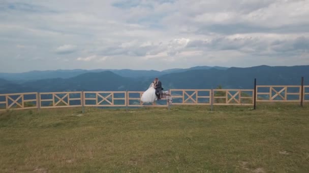 Bräutigam und Braut sitzen auf dem Zaun in der Nähe der Berghügel. Drohnenschuss aus der Luft