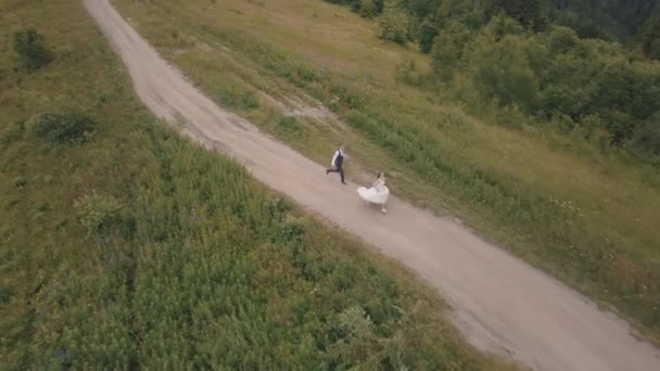 Le marié court avec la mariée sur les collines montagneuses. Vue aérienne du drone — Video