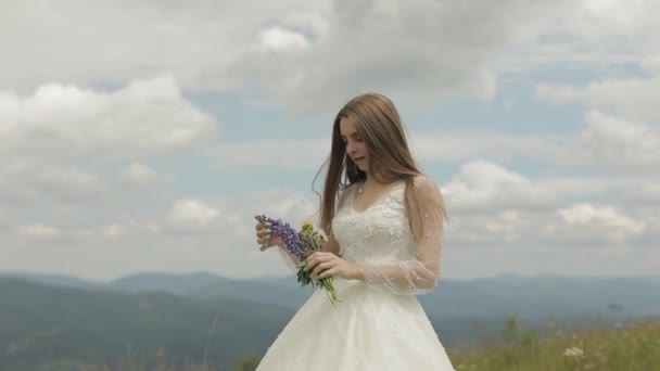 Hermosa novia en vestido de novia estancia en las montañas con ramo de flores — Vídeos de Stock