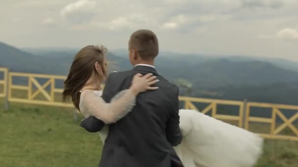 A vőlegény menyasszonyt tart a karjaiban, hegyi dombokon. Esküvői pár. Boldog család — Stock videók