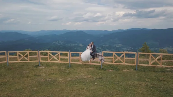 Vőlegény a menyasszony ülni a kerítés közelében hegyi dombok. Légi drone lövés — Stock Fotó