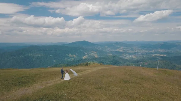 Ο γαμπρός με τη νύφη να περπατάει μαζί σε ορεινούς λόφους. Εναέρια βολή — Φωτογραφία Αρχείου