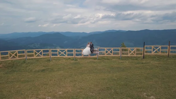 Vőlegény a menyasszony ülni a kerítés közelében hegyi dombok. Légi drone lövés — Stock Fotó