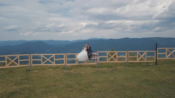 Vőlegény a menyasszony ülni a kerítés közelében hegyi dombok. Légi drone lövés — Stock Fotó