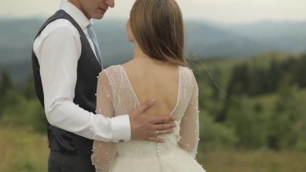 El novio acaricia a las novias cerca de las colinas de la montaña. Pareja de boda — Vídeo de stock