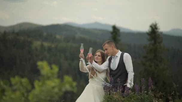 El novio con la novia beben el champán en las colinas montañosas. Pareja de bodas. Familia — Vídeos de Stock