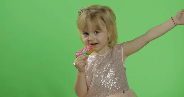 Menina em vestido brilhante começa a comer biscoitos na forma de morangos — Fotografia de Stock