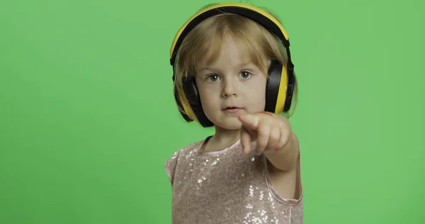 Flicka i glänsande klänning och hörlurar Lyssna på musik och visar ett finger framåt — Stockfoto
