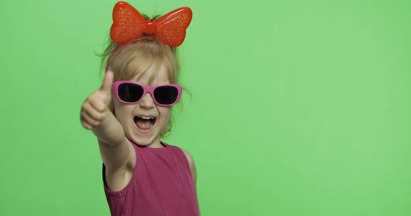 Chica positiva en vestido morado, gafas de sol y cinta roja. Sonríe. Pulgares arriba — Foto de Stock