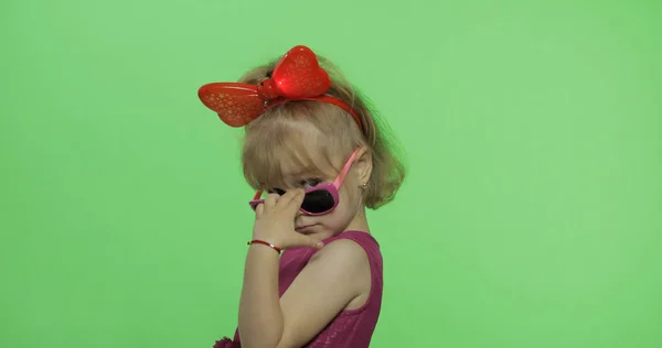 Positiv tjej i lila klänning, solglasögon och rött band tittar på kamera — Stockfoto