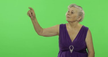 Yaşlı bir kadın bir şeyi işaret ediyor ve gülümsüyor. Yaşlı büyükanne. Chroma anahtarı