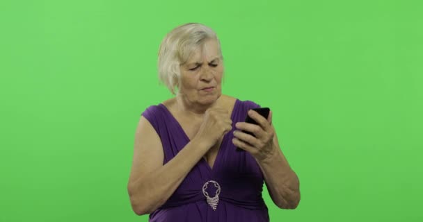 Starsza kobieta pracuje na smartfonie. Stara babcia uśmiecha się. Klucz chrominancji — Wideo stockowe