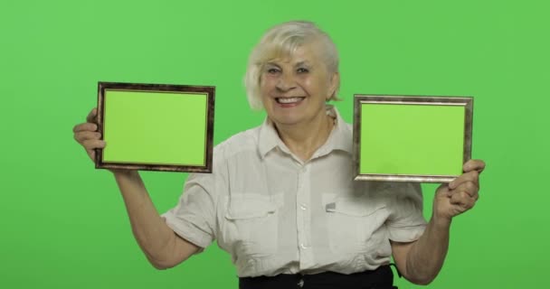 Μια ηλικιωμένη γυναίκα που κρατά δύο καρέ με πράσινη εικόνα. Γιαγιά. Πλήκτρο αποχρώσεων — Αρχείο Βίντεο