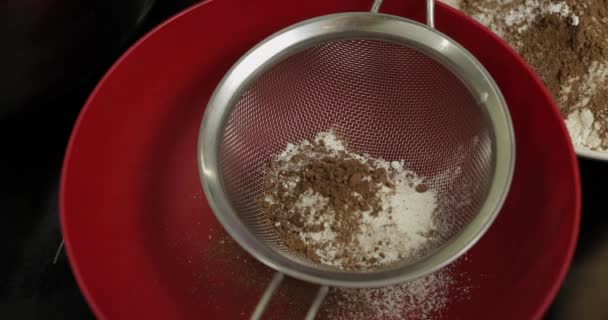 女の子はテーブルの上に小麦粉でボウルにココアパウダーをふるう手。トップビュー — ストック動画