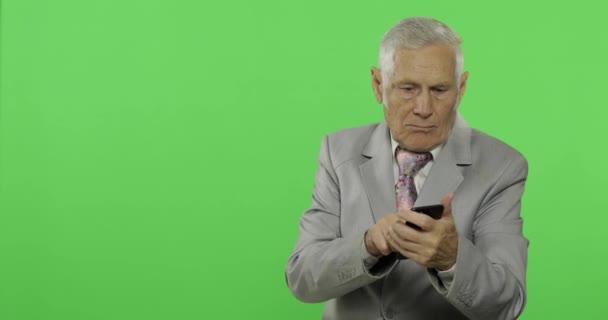 Handsome elderly businessman texting on smartphone and points at something — Stock Video