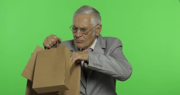 買い物袋を持つ高齢のビジネスマン。買い物の後にフォーマルな服装の老人 — ストック動画
