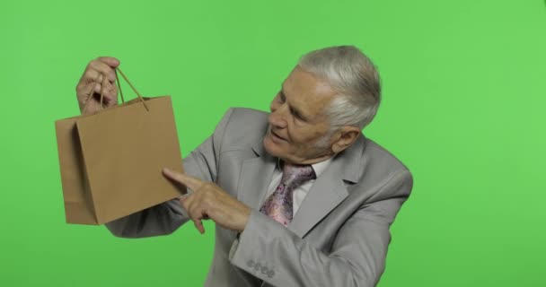 Пожилой человек с сумкой. Смотрит в камеру и растягивает подарок. — стоковое видео