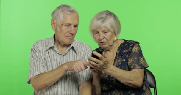 Ηλικιωμένος άντρας και γυναίκα που κάθονται μαζί και εργάζονται σε smartphone. Πλήκτρο αποχρώσεων — Αρχείο Βίντεο