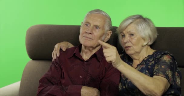 Мужчина и женщина старшего возраста сидят вместе на диване и смотрят телевизор. Ключ хрома — стоковое видео
