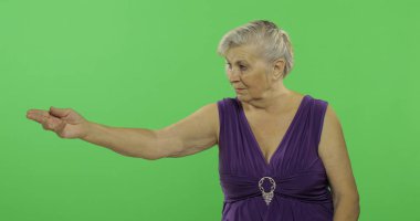 Yaşlı bir kadın bir şeyi işaret ediyor ve gülümsüyor. Yaşlı büyükanne. Chroma anahtarı
