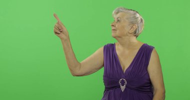 Yaşlı bir kadın bir şeyi işaret ediyor ve gülümsüyor. Yaşlı büyükanne. Chroma anahtarı