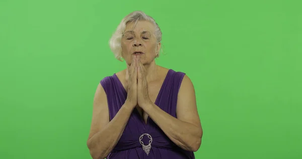 Una donna anziana prega con le mani giunte. Vecchia nonna. Chiave cromatica — Foto Stock